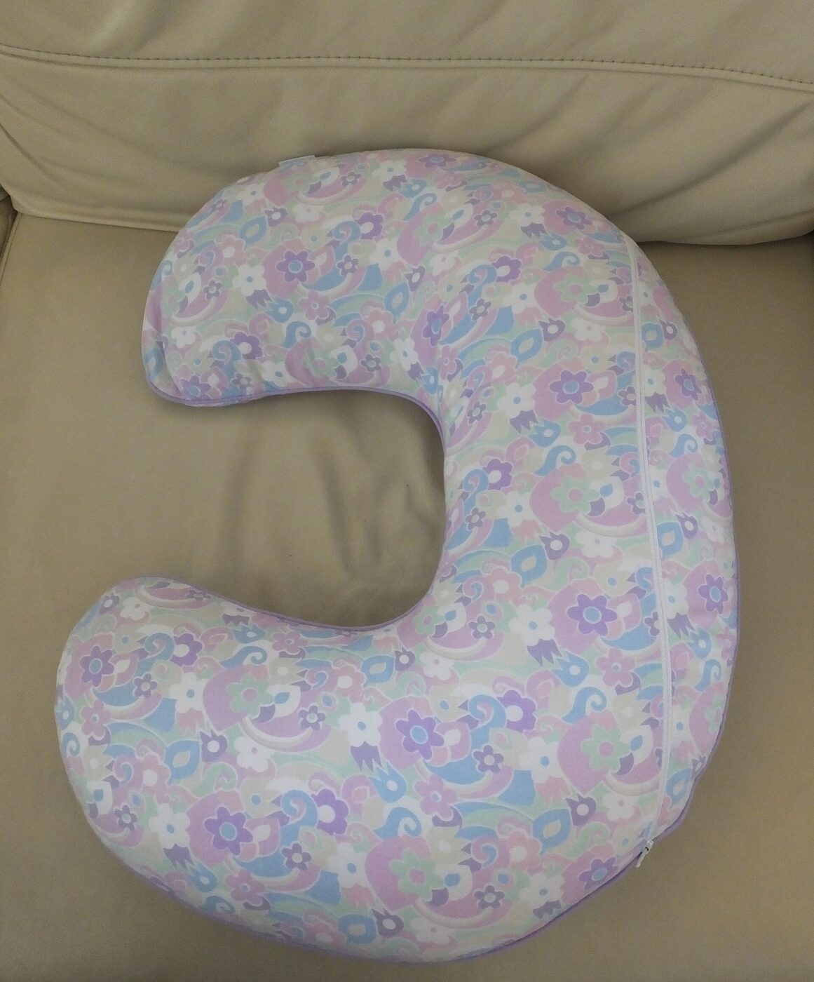 A C-shaped nursing pillow in a pastel floral cover resting on a couch.