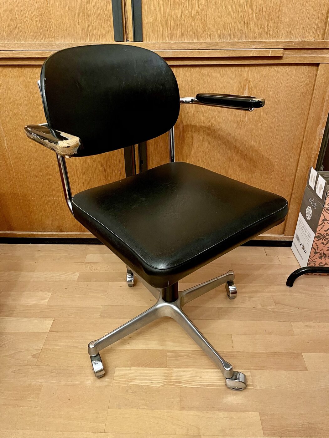 A black vinyl swivel desk chair with padded armrests on a five-star caster base.