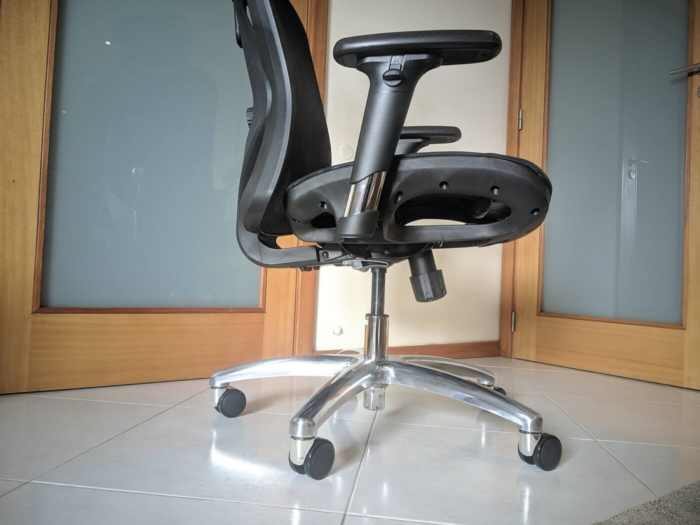 A black mesh office chair with adjustable armrests on a polished aluminum five-star base