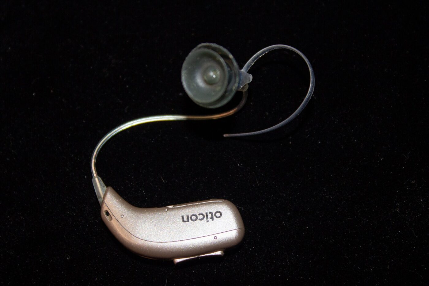 A small behind-the-ear hearing aid with a thin cable leading to a soft dome ear tip