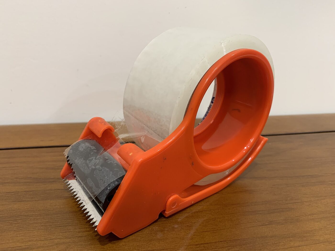 An orange gun dispenser holding clear plastic packing tape with the cutter exposed.