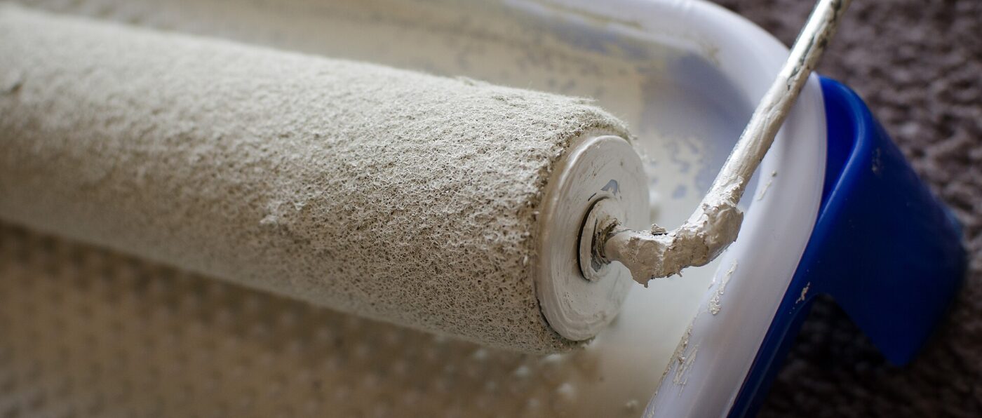 Paint roller coated in pale paint resting in a plastic paint tray