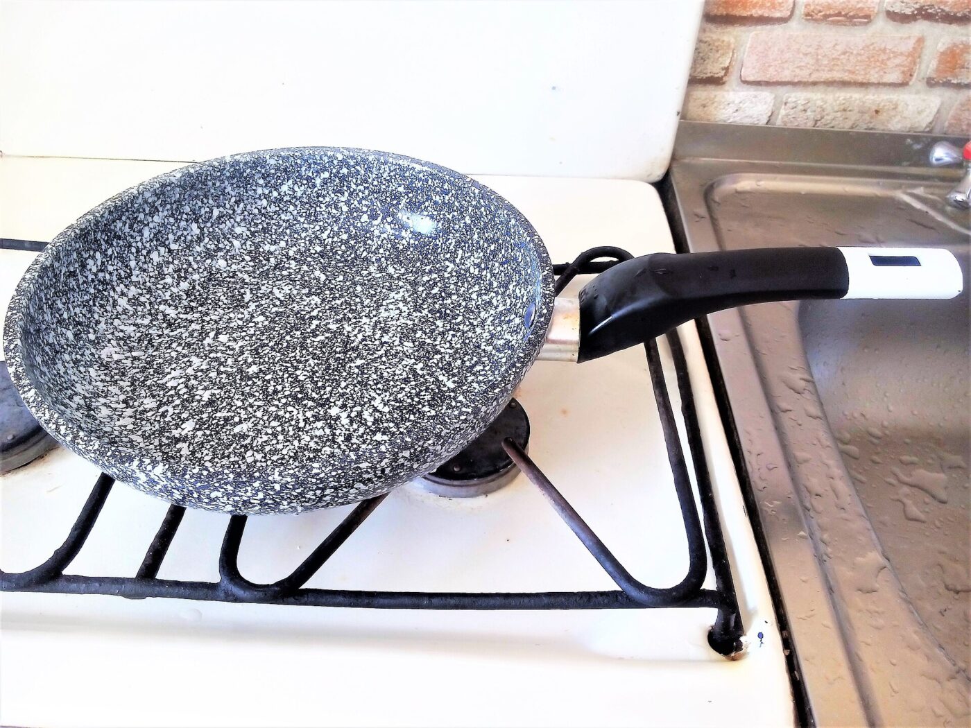 A speckled stone-look nonstick frying pan resting on the grate of a white gas stove