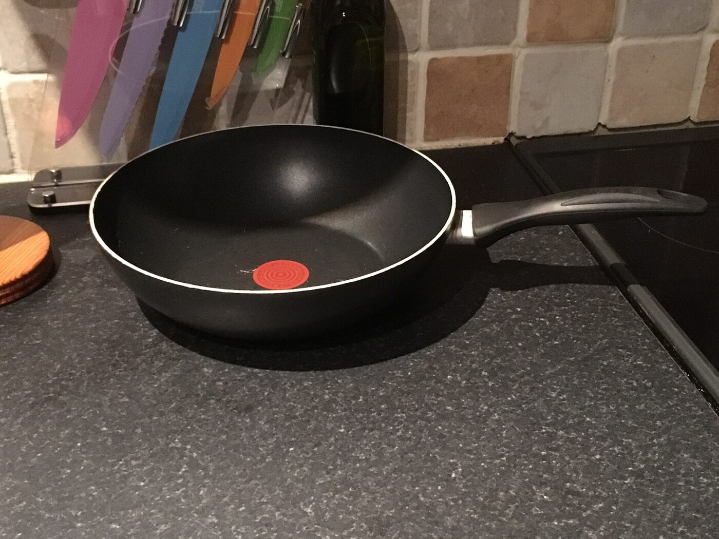 A black nonstick frying pan with a red heat-indicator spot sitting on a kitchen countertop