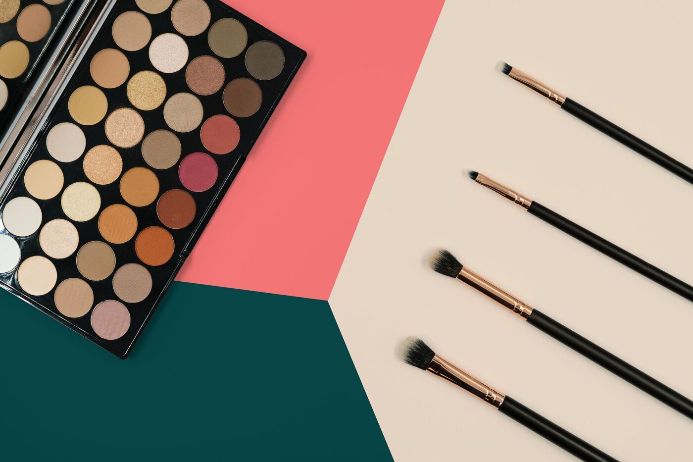An open eyeshadow palette of neutral shades beside a row of makeup brushes