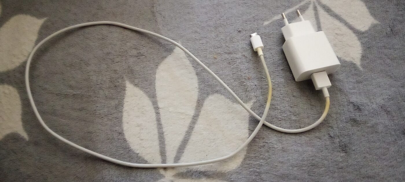 A white USB wall charger with its cable coiled on a stone surface.