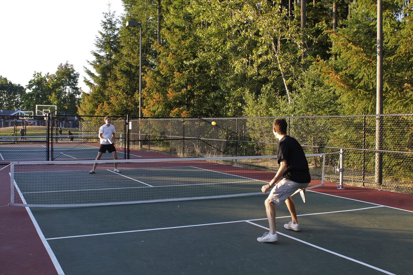Two players trade shots across the net on an outdoor pickleball court as the ball flies in midair