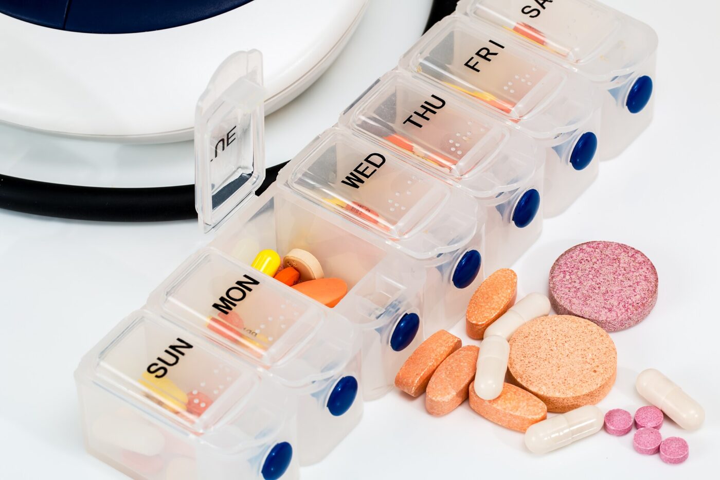 A clear weekly pill organizer with a compartment for each day and loose tablets beside it