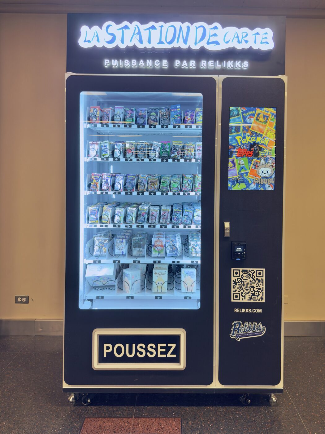 A trading card vending machine stocked with booster packs, with Pokémon artwork on its side screen