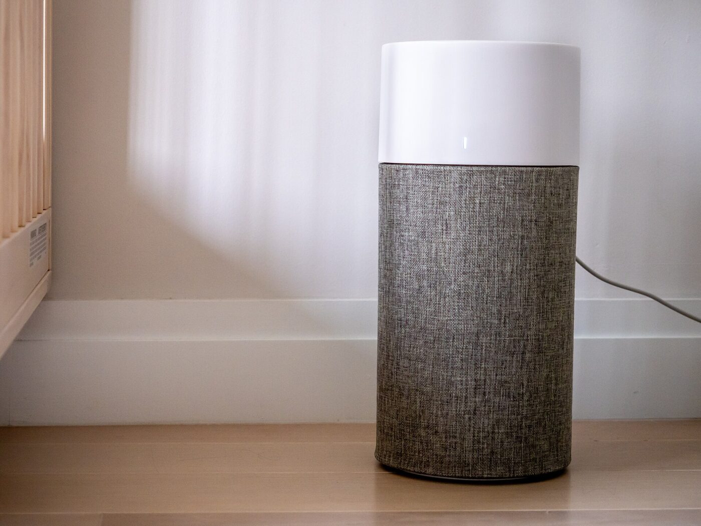A small cylindrical air purifier with a fabric-covered body, standing on a wood floor.