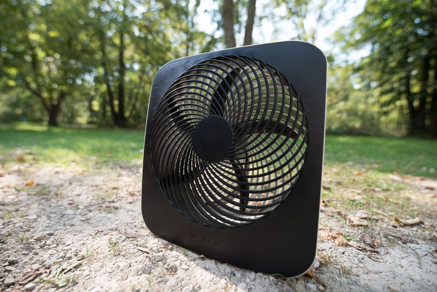 A battery-powered portable fan of the kind sold for camping, standing outdoors on gravel.