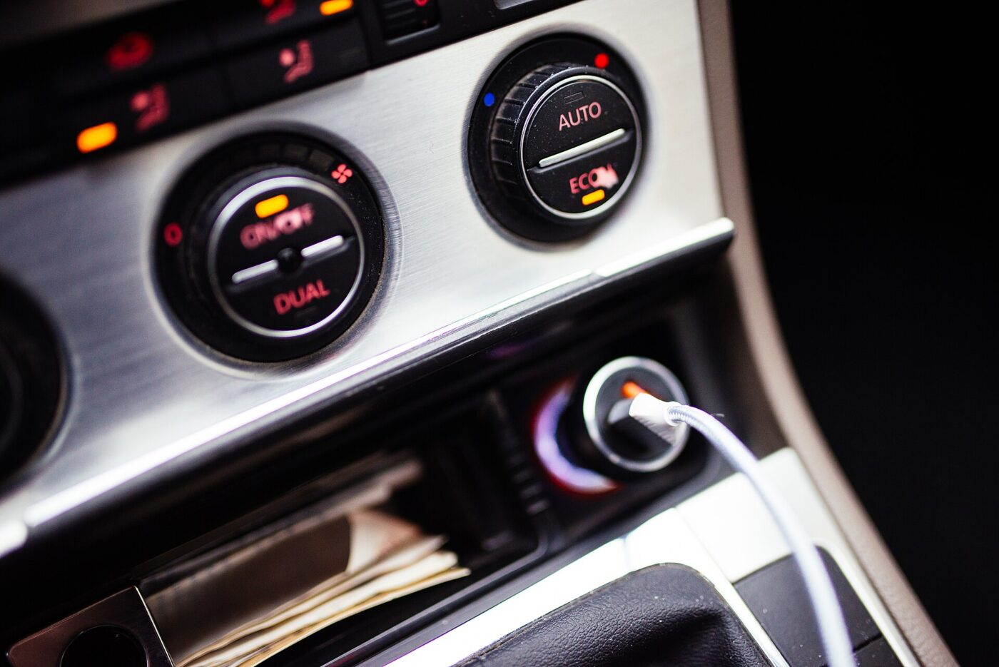 A cable plugged into a car's accessory socket next to the dashboard climate controls.