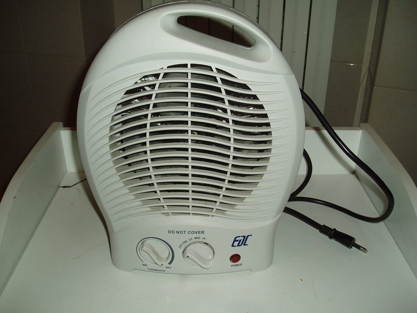 A white portable fan heater with two control dials and its power cord coiled alongside.