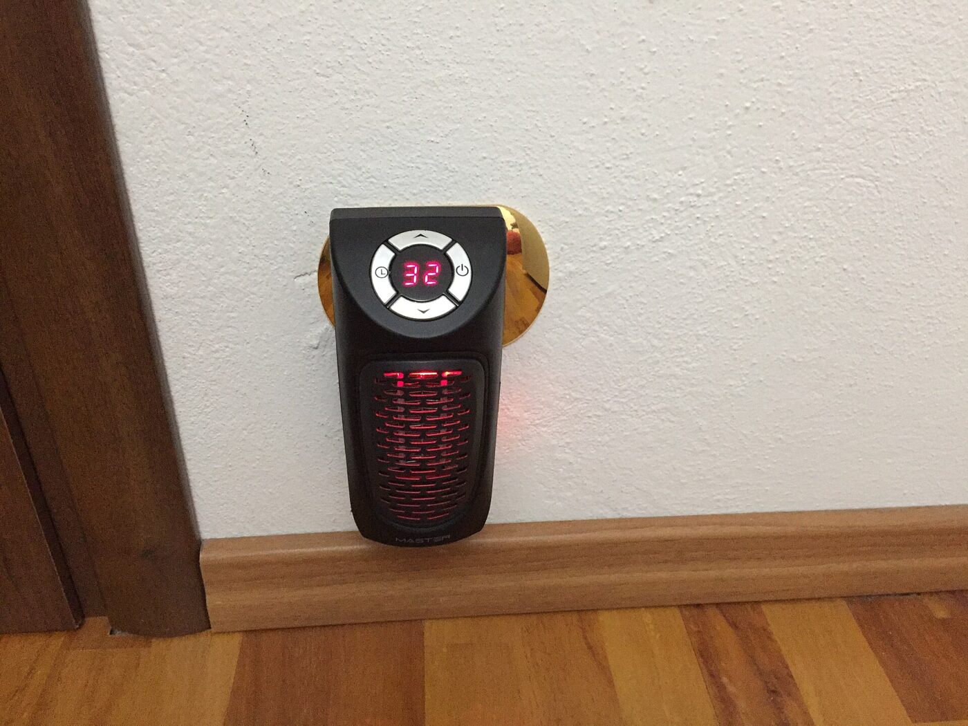 A plug-in mini heater in a wall socket, its digital display showing a set temperature.