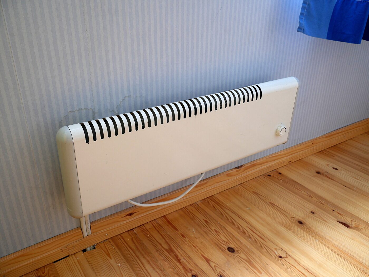 A slim white electric panel heater standing against a wall on a wooden floor.
