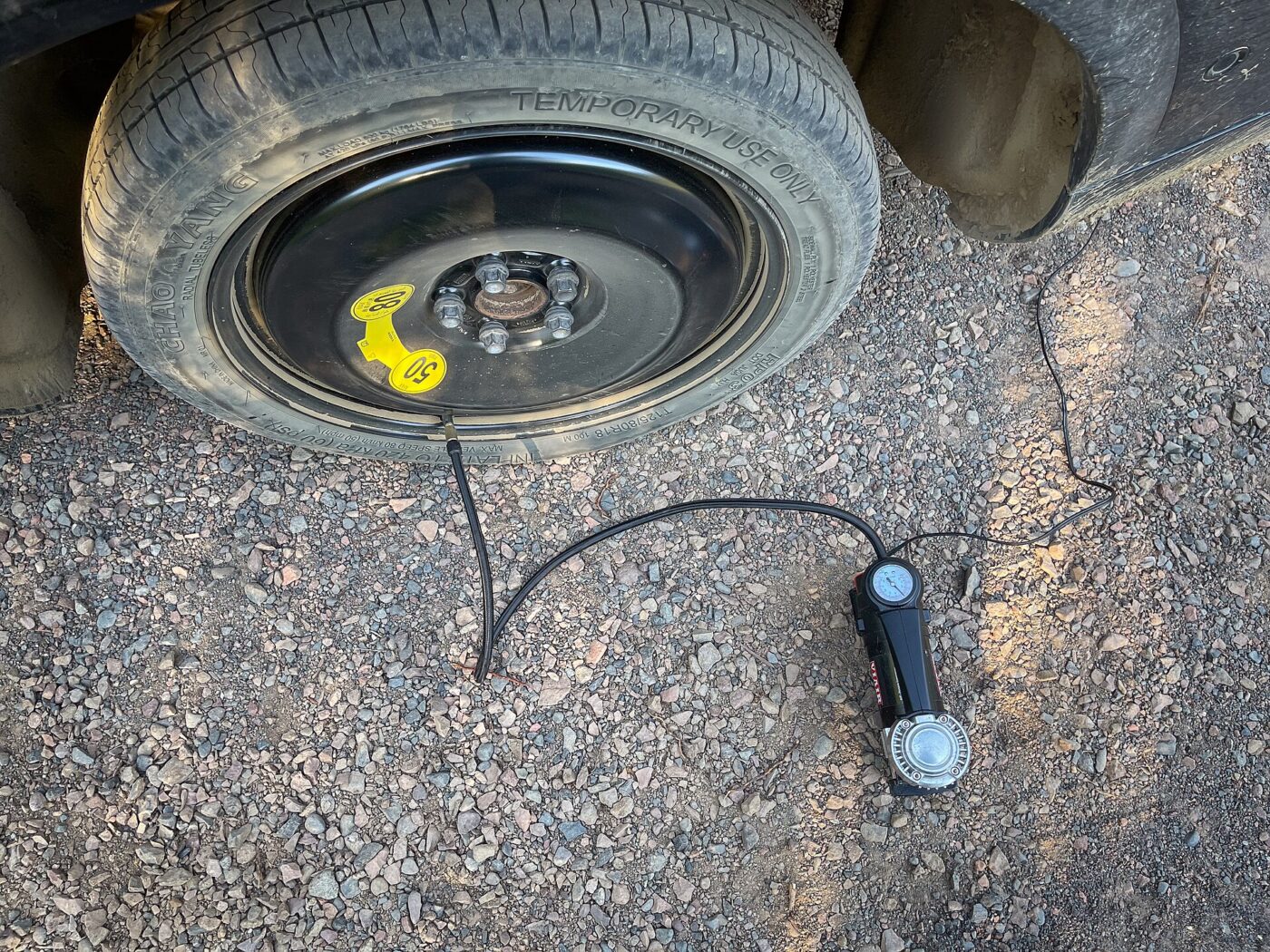 A small portable inflator connected by a hose to a compact spare tire on pavement