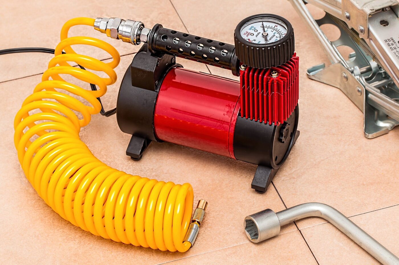A red portable air compressor with a coiled yellow air hose and pressure gauge