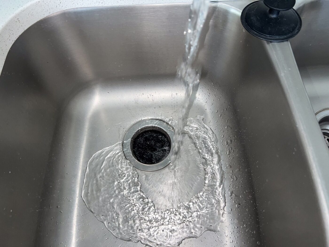 Water running from a kitchen tap into a stainless steel sink and its open drain.