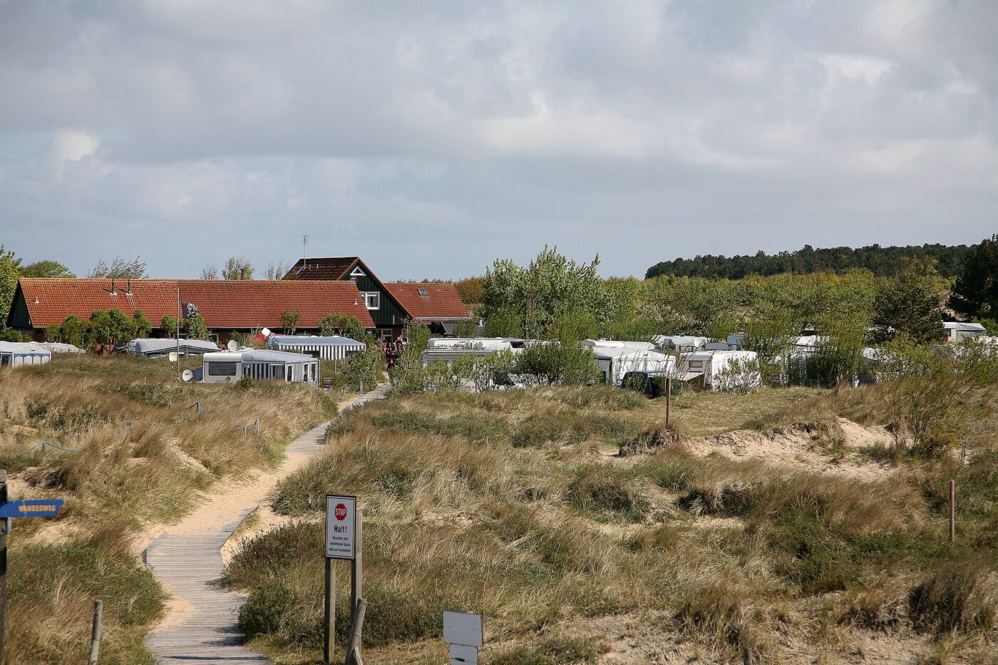Rows of caravans and motorhomes parked at a coastal campground behind a sandy path.