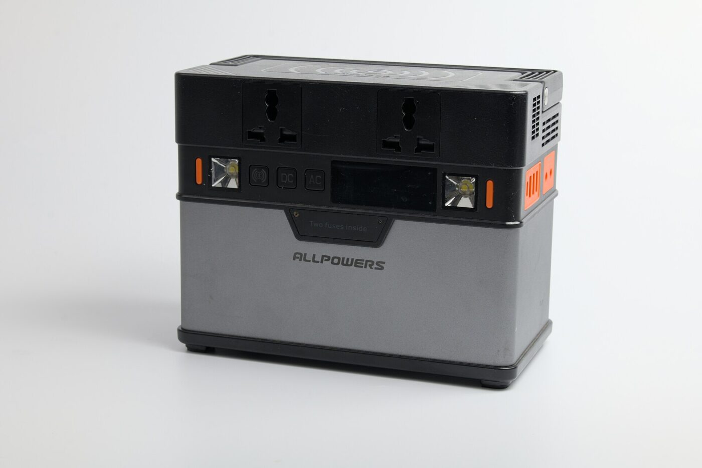 A compact portable power station with two AC sockets, a small display and side lights, on a white background