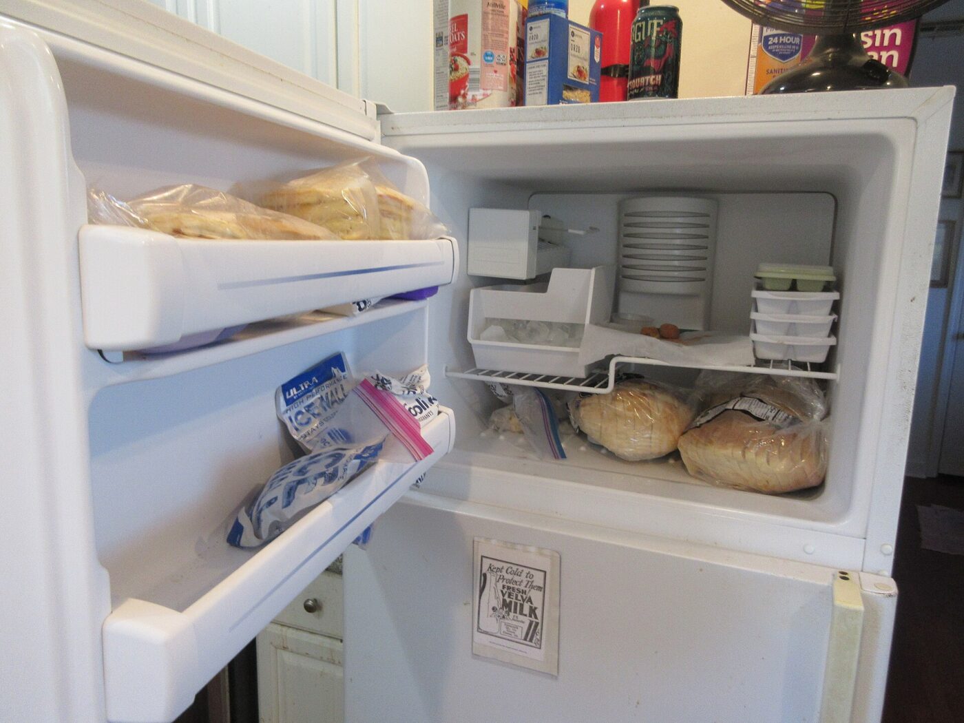An open freezer compartment on a home refrigerator, stocked with bread and plastic containers.