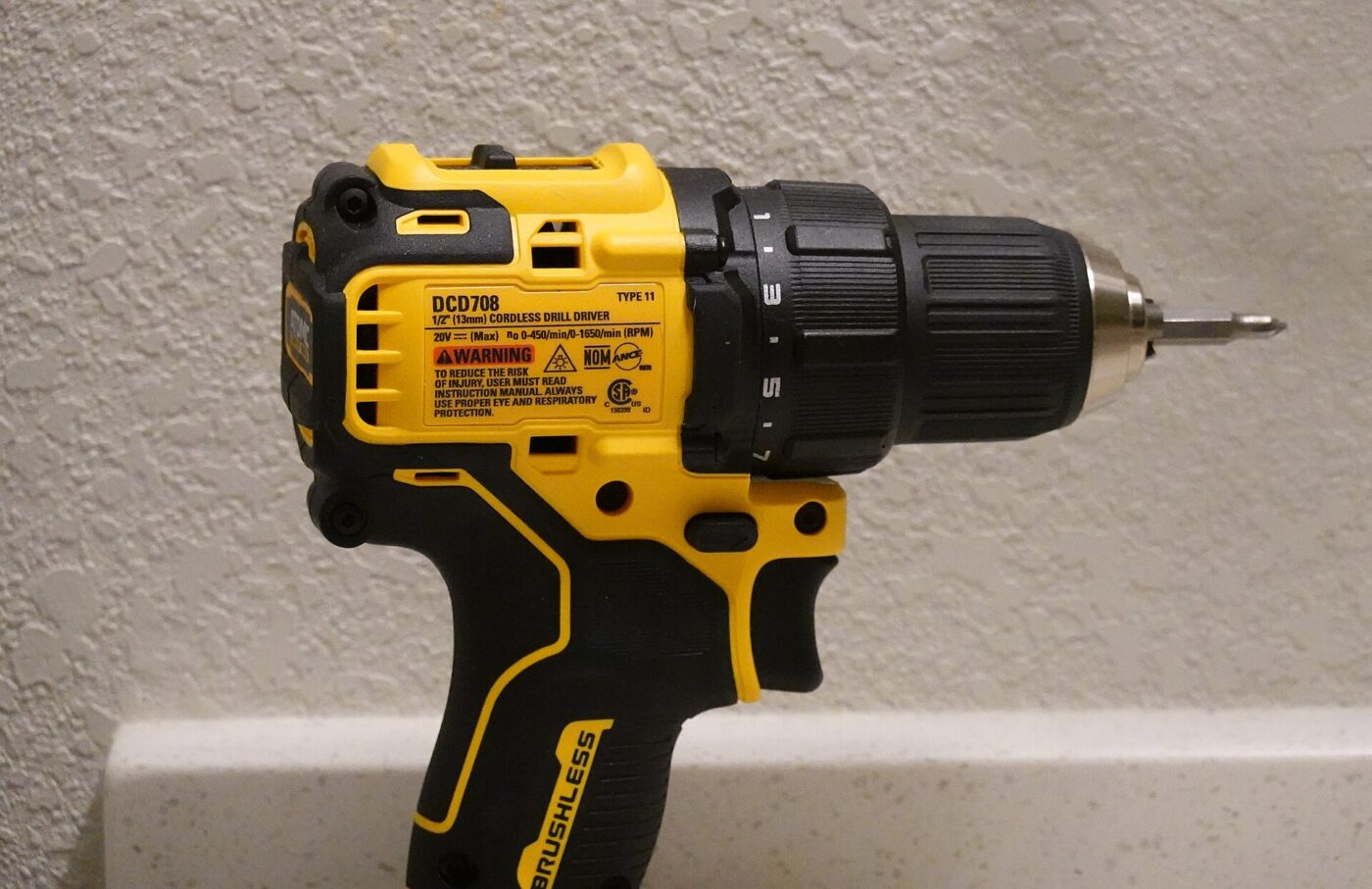 Yellow and black brushless cordless drill driver standing on a counter against a textured wall