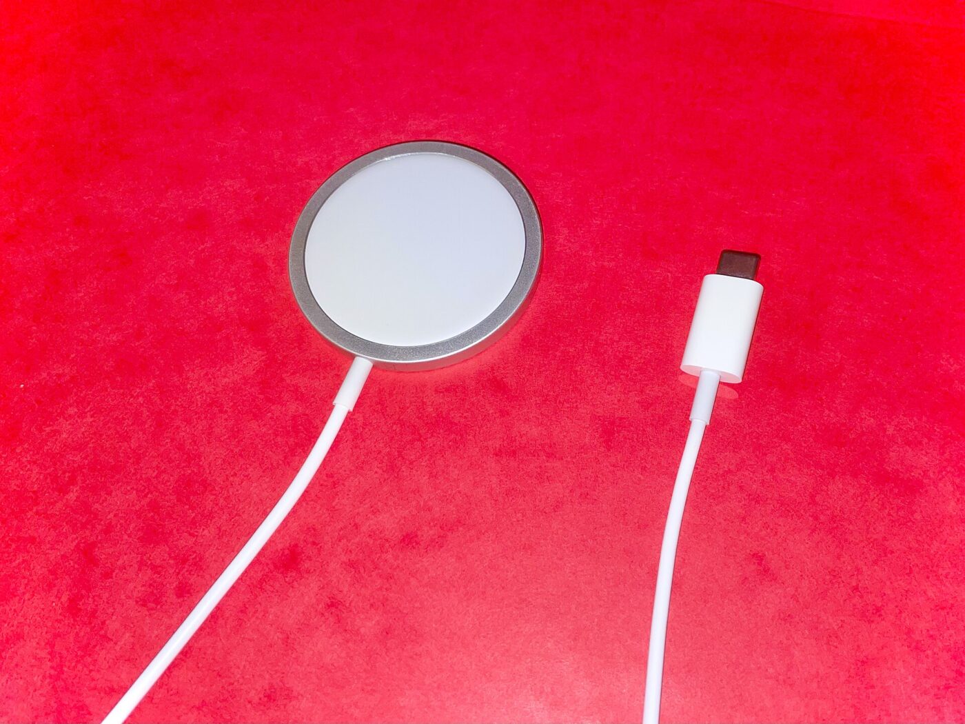 Round white wireless charging puck with a USB-C cable lying on a bright red surface