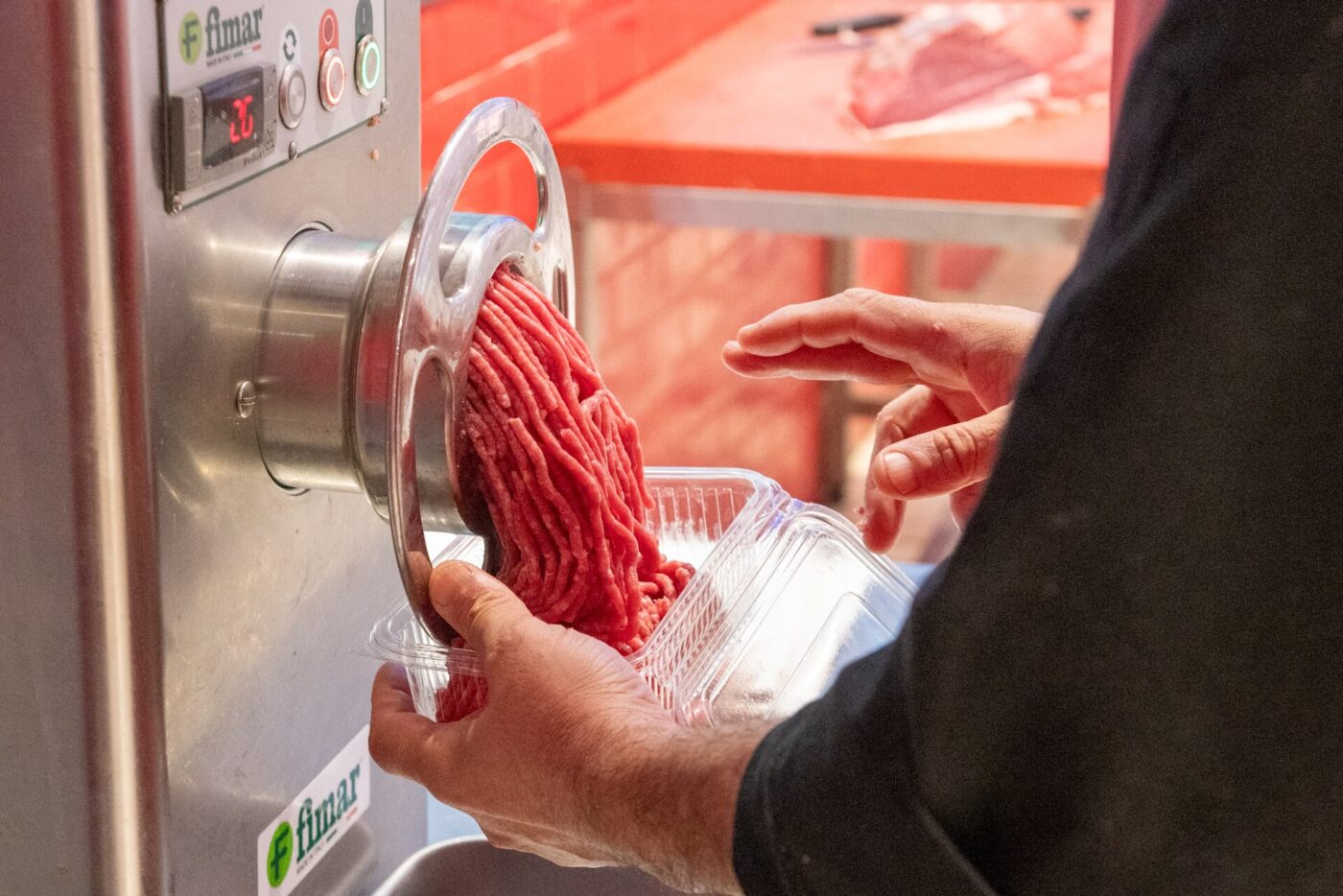 Fresh ground beef coming out of a stainless steel meat grinder into a plastic tray
