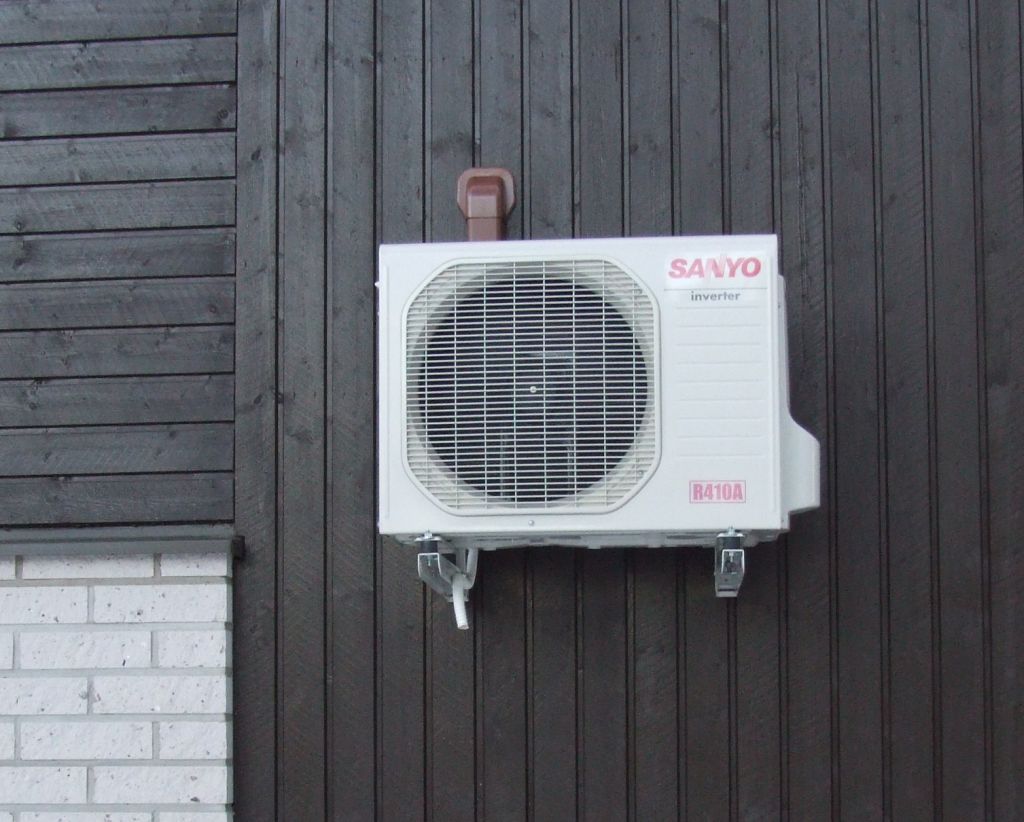 Wall-mounted outdoor unit with an R410A refrigerant label, fixed to a dark wooden wall