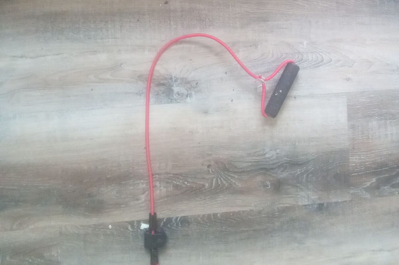 A red resistance tube attached to a black handle, lying on a wood floor.
