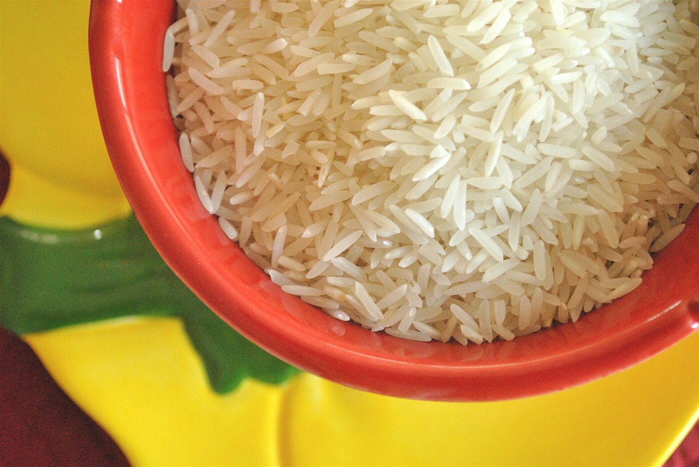 Raw long-grain white rice filling a bright red and yellow plastic bowl