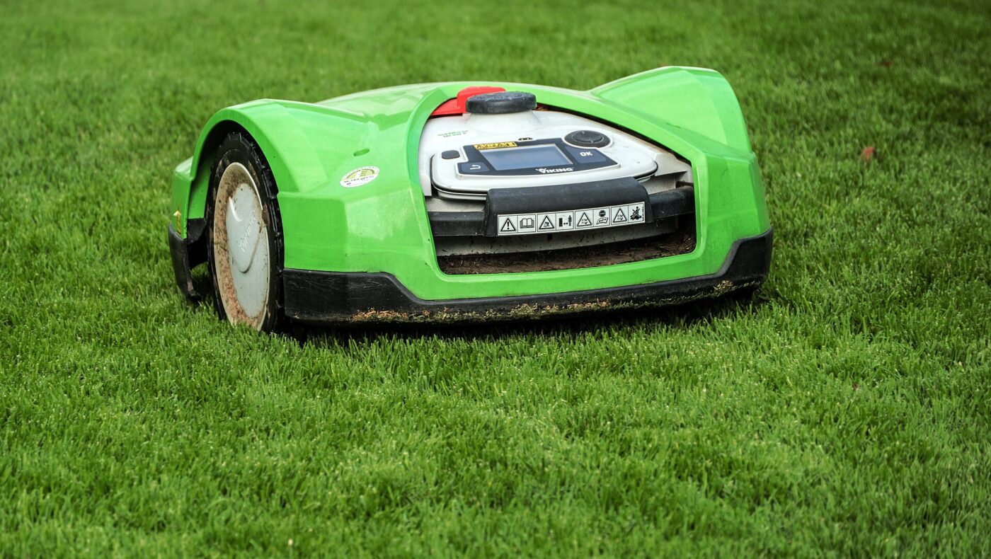 A green robotic lawn mower working on a short, freshly trimmed grass lawn
