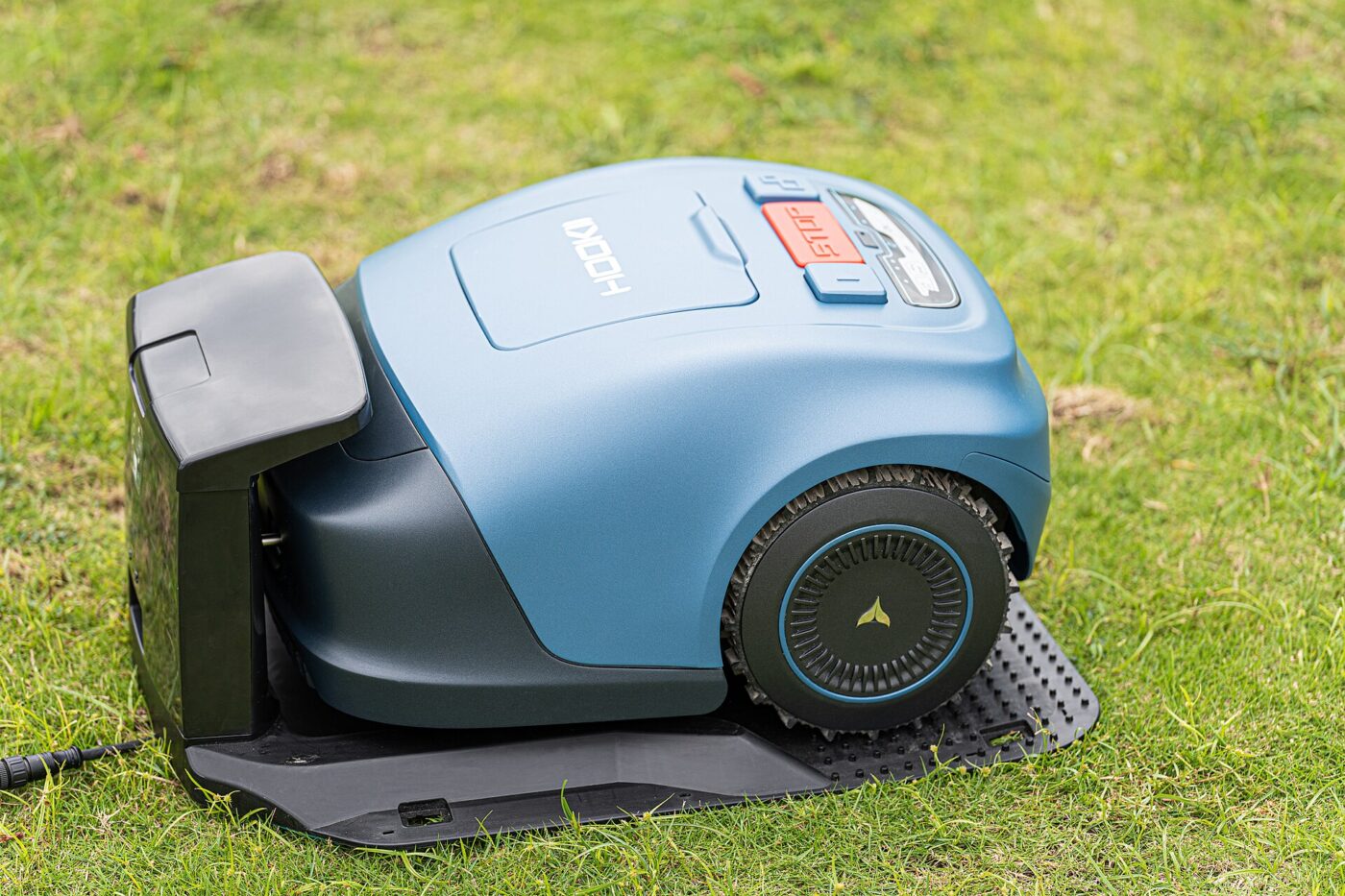 A blue robotic lawn mower parked on its charging dock on a grassy lawn