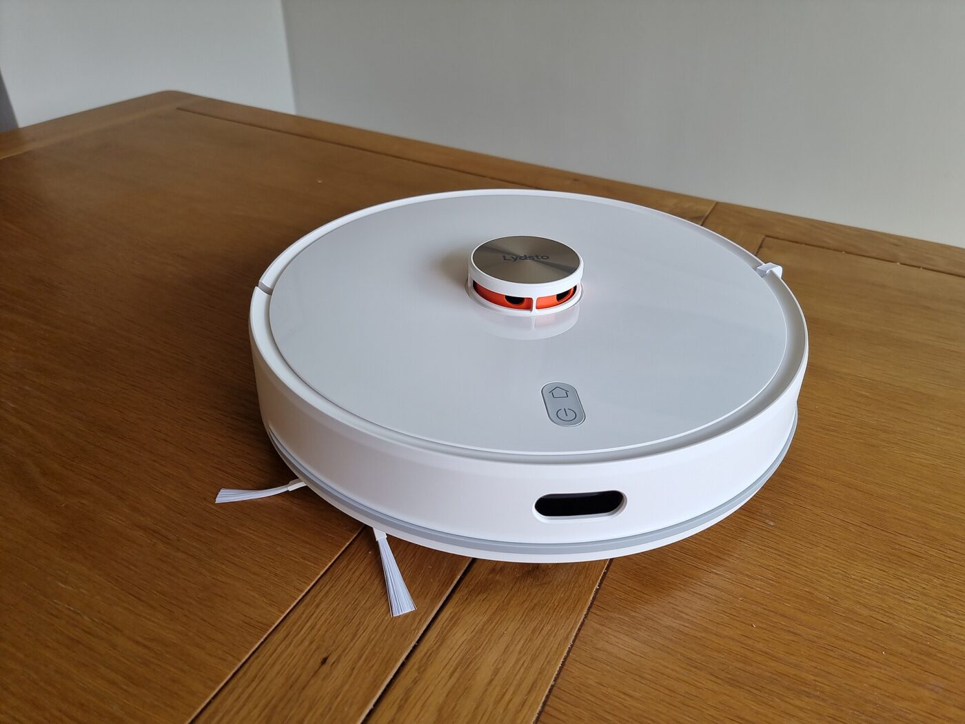 A white robot vacuum with a round sensor turret on top, sitting on a wooden table