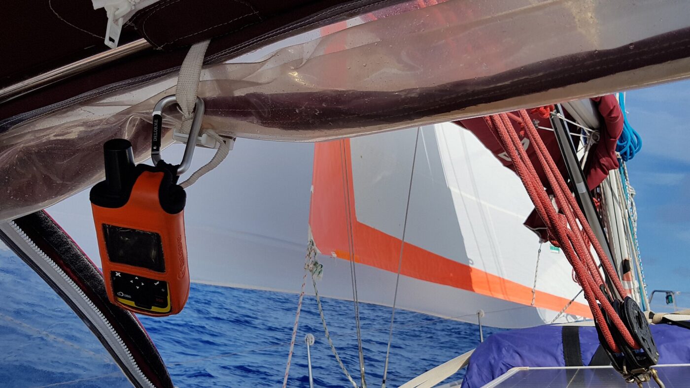 An orange handheld satellite messenger clipped to a sailboat's rigging above open water