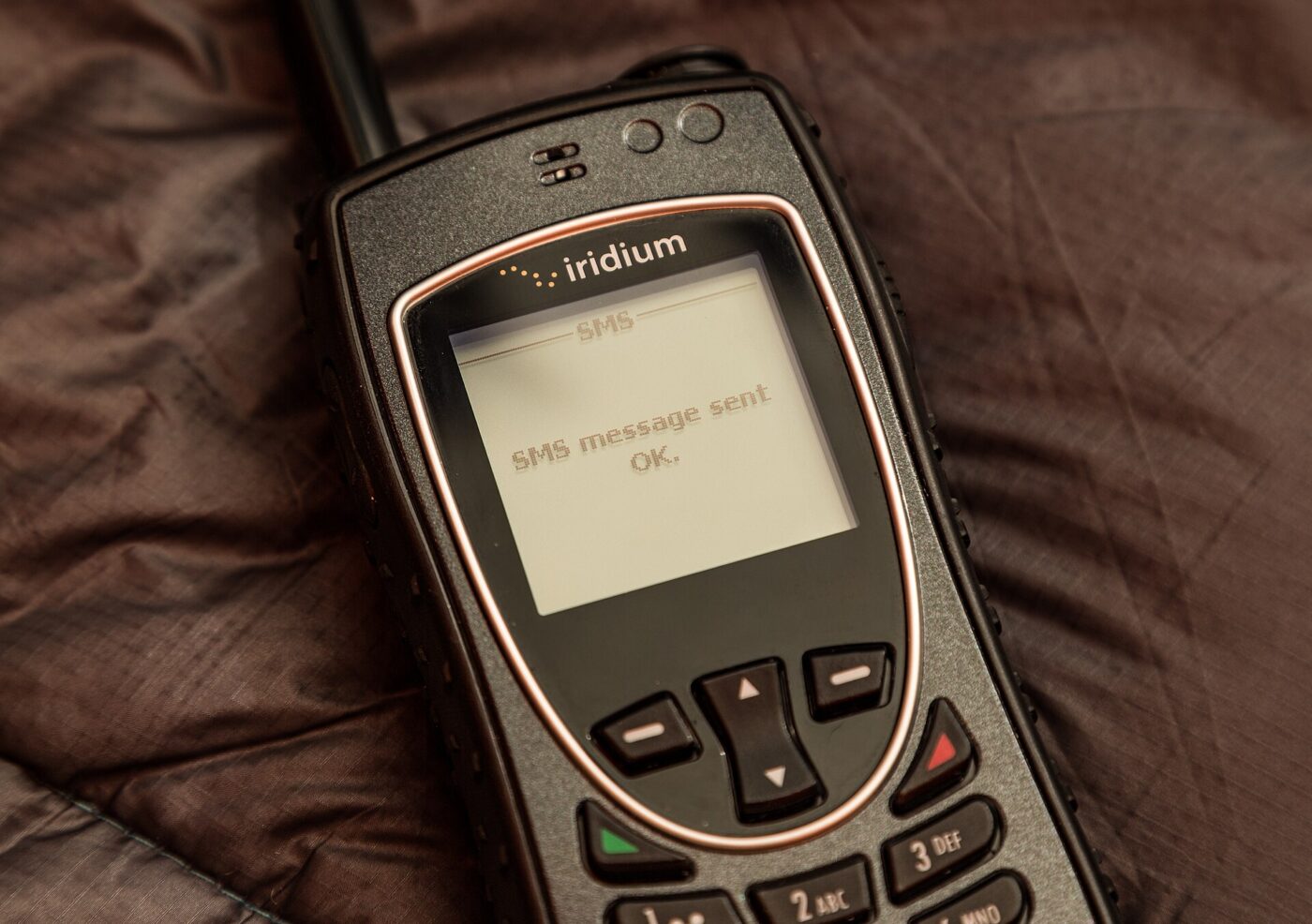 A handheld satellite phone lying on a leather seat, its small screen showing a text message