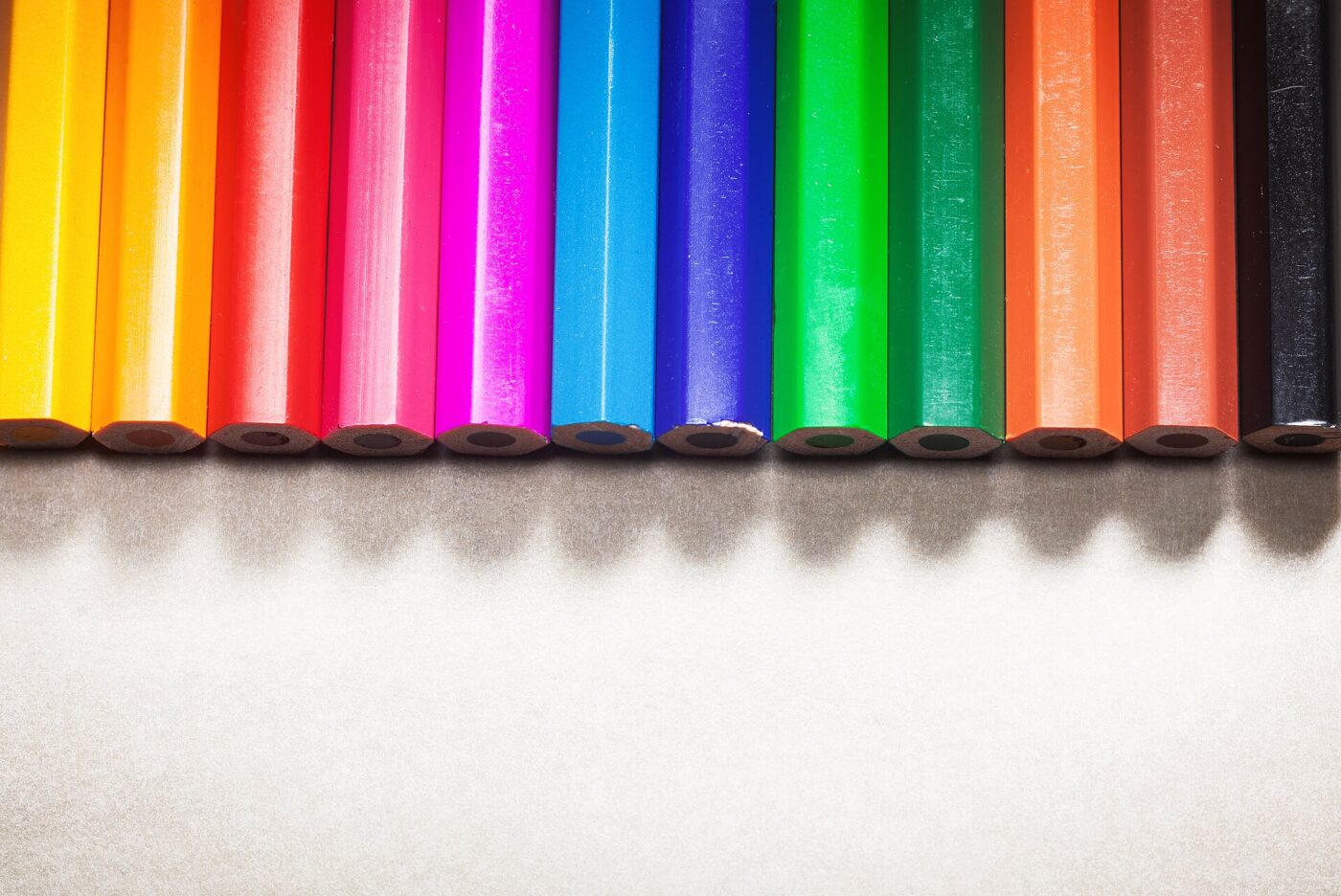 Wood-cased colored pencils lined up side by side on a light surface.