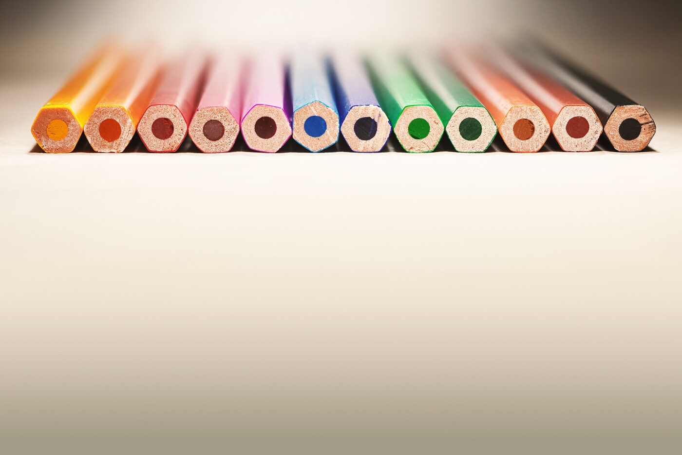 A row of wood-cased colored pencils seen end-on against a plain pale background.