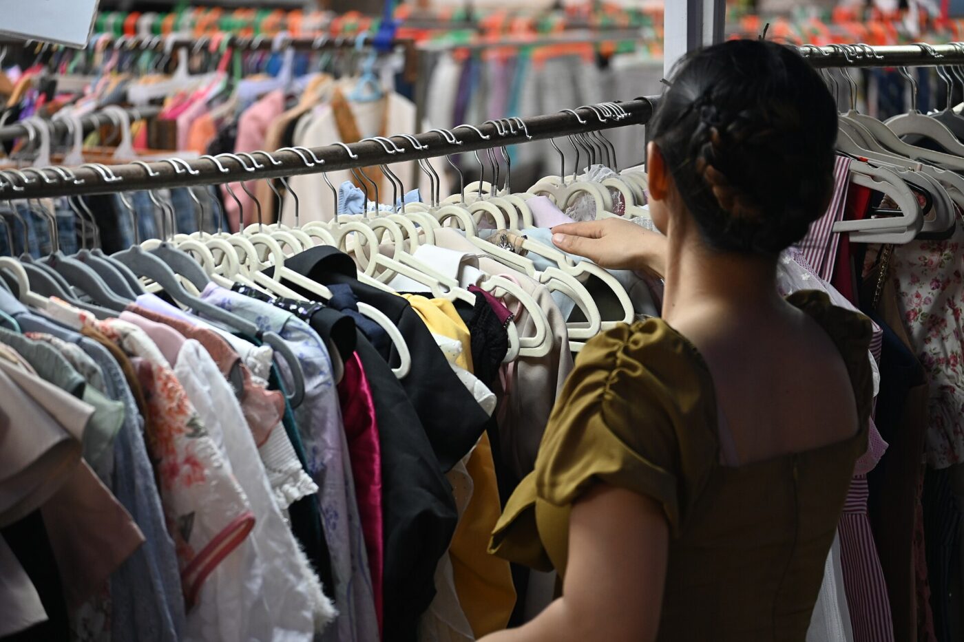 A shopper browses a crowded rack of dresses and tops on plastic hangers