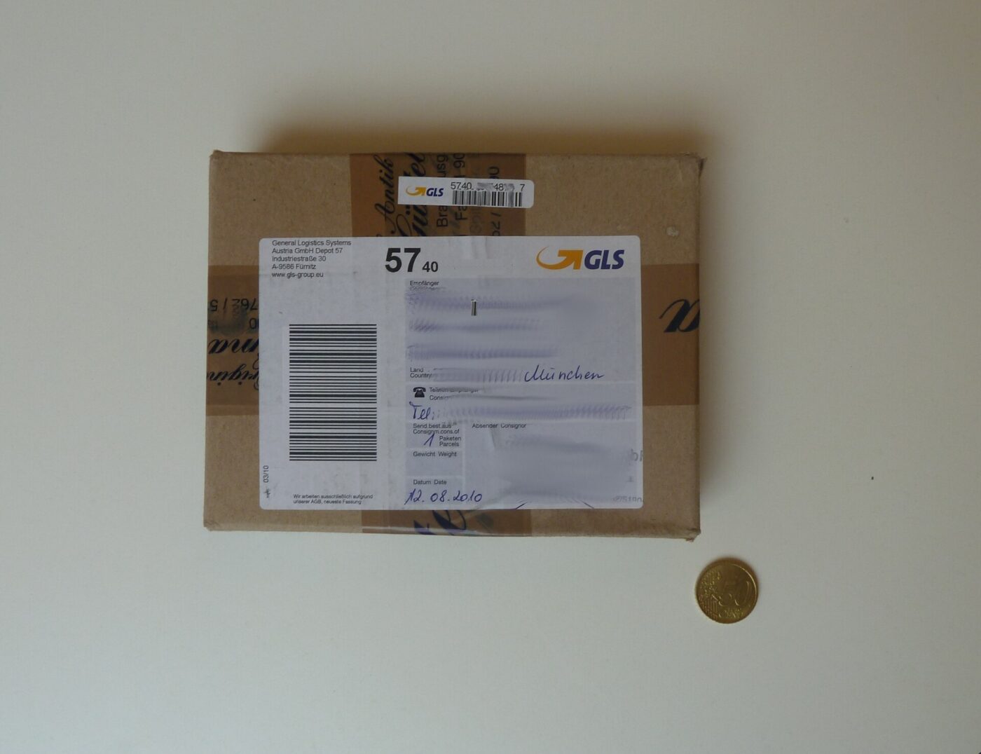 A small cardboard parcel with a printed carrier label and a coin for scale