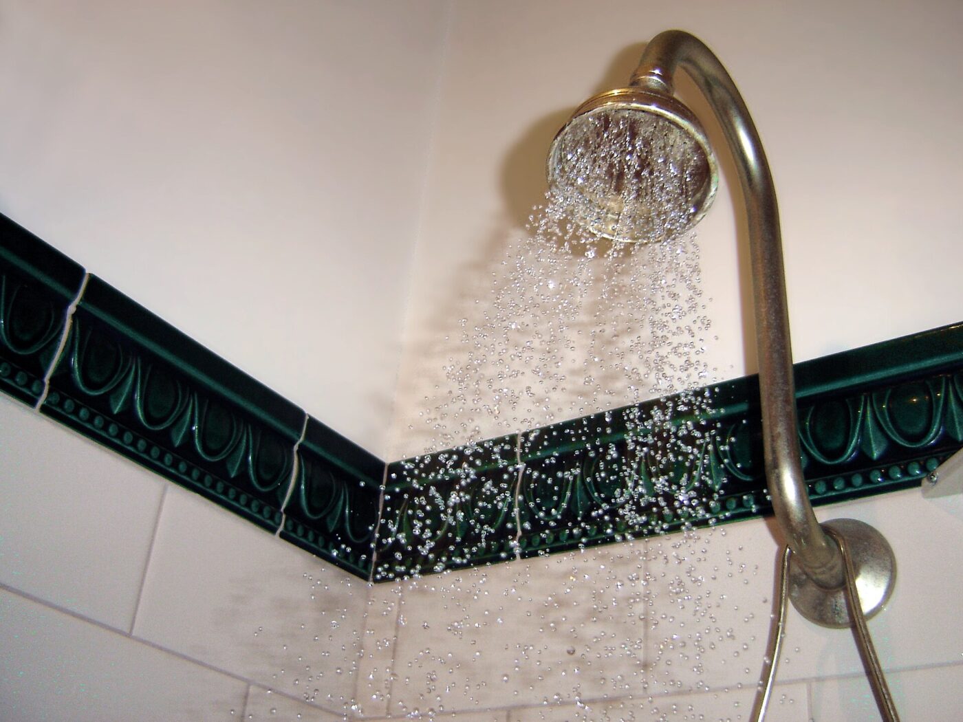 A fixed chrome showerhead on a curved arm above a tiled shower wall