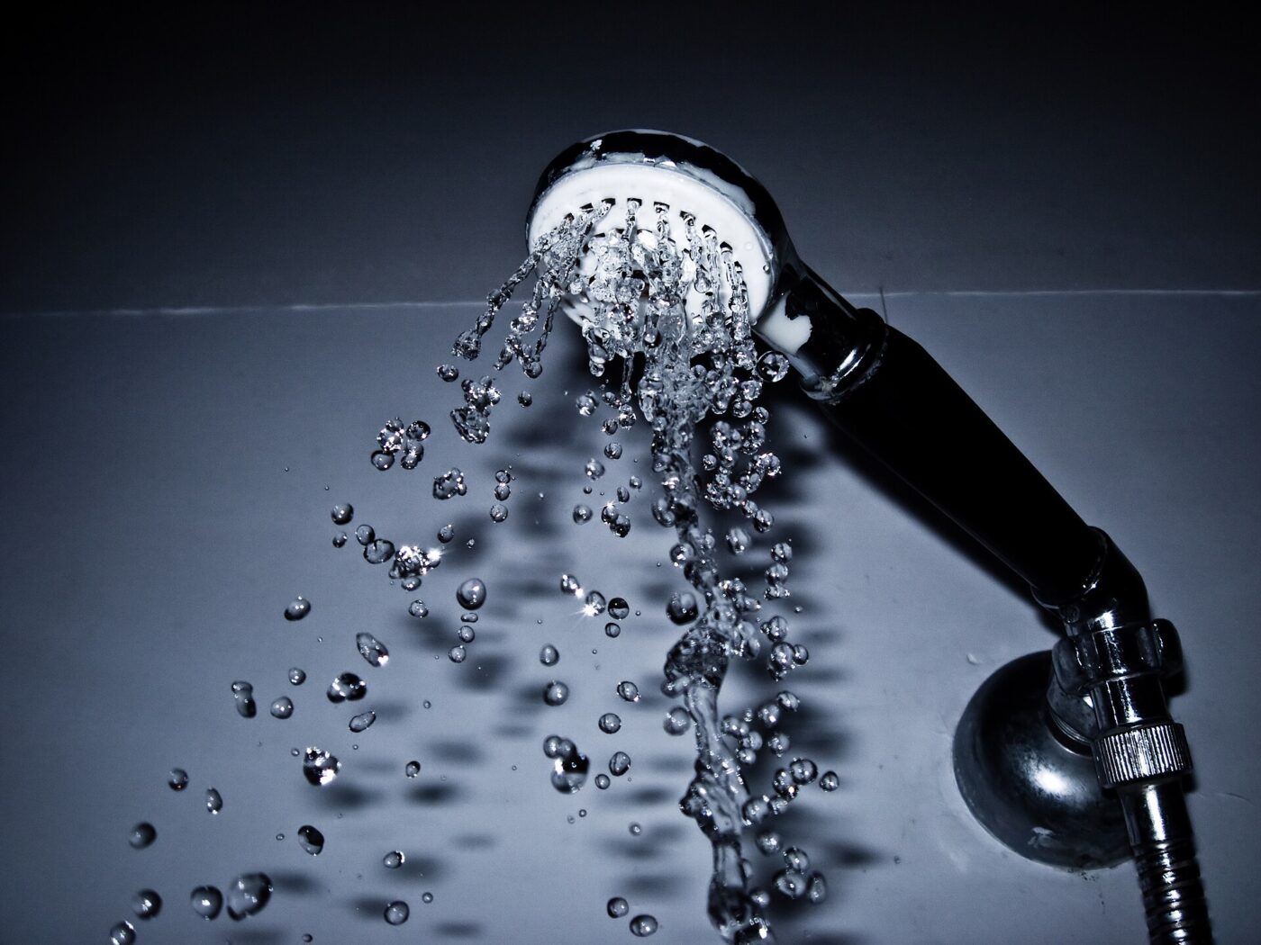 A handheld showerhead spraying water, photographed against a dark studio background