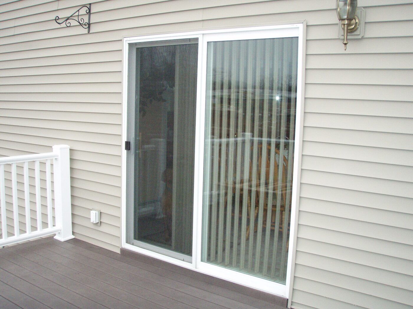 A white vinyl sliding patio door and its screen panel, seen from a backyard deck.