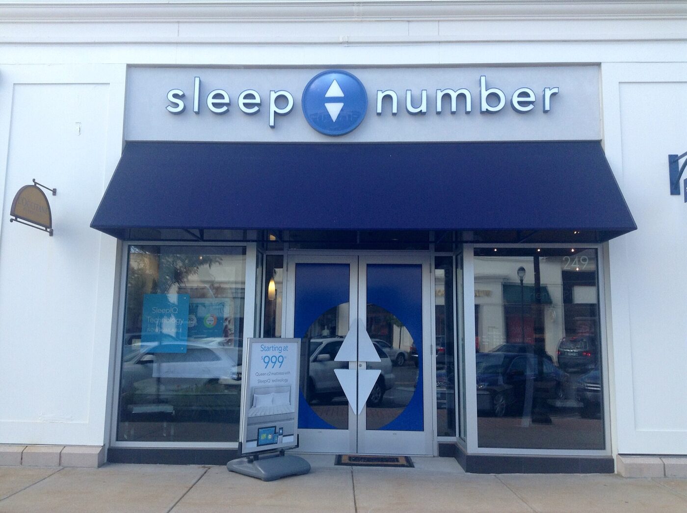 The entrance of a Sleep Number store, with a blue awning and a price sign by the door
