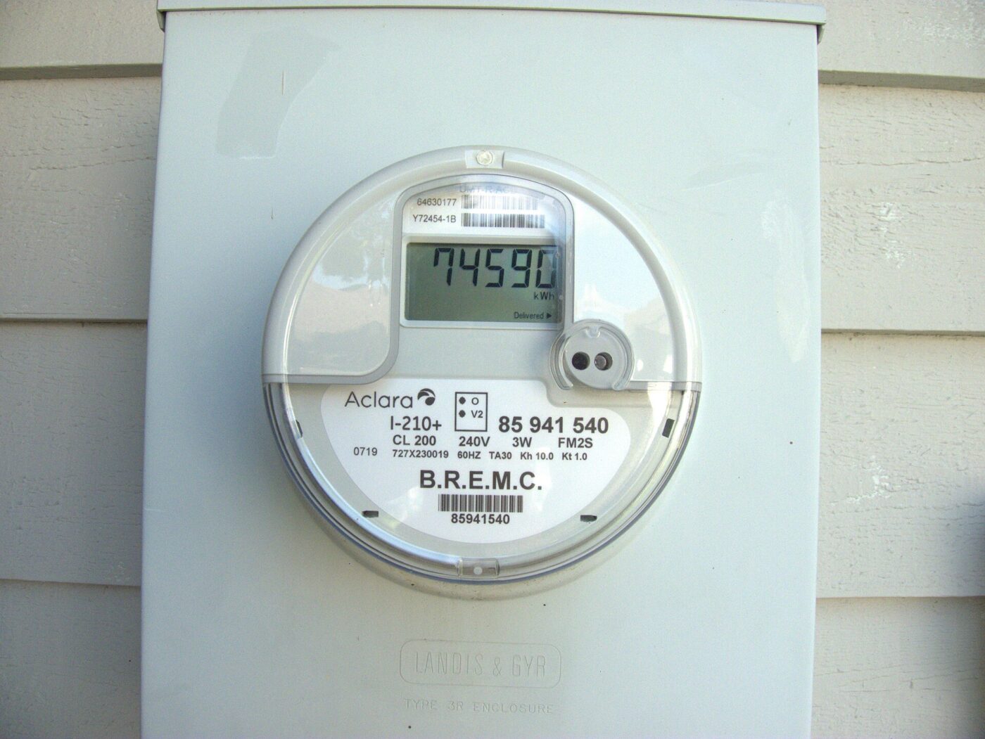 A digital electricity meter mounted on the outside wall of a house, showing a reading.