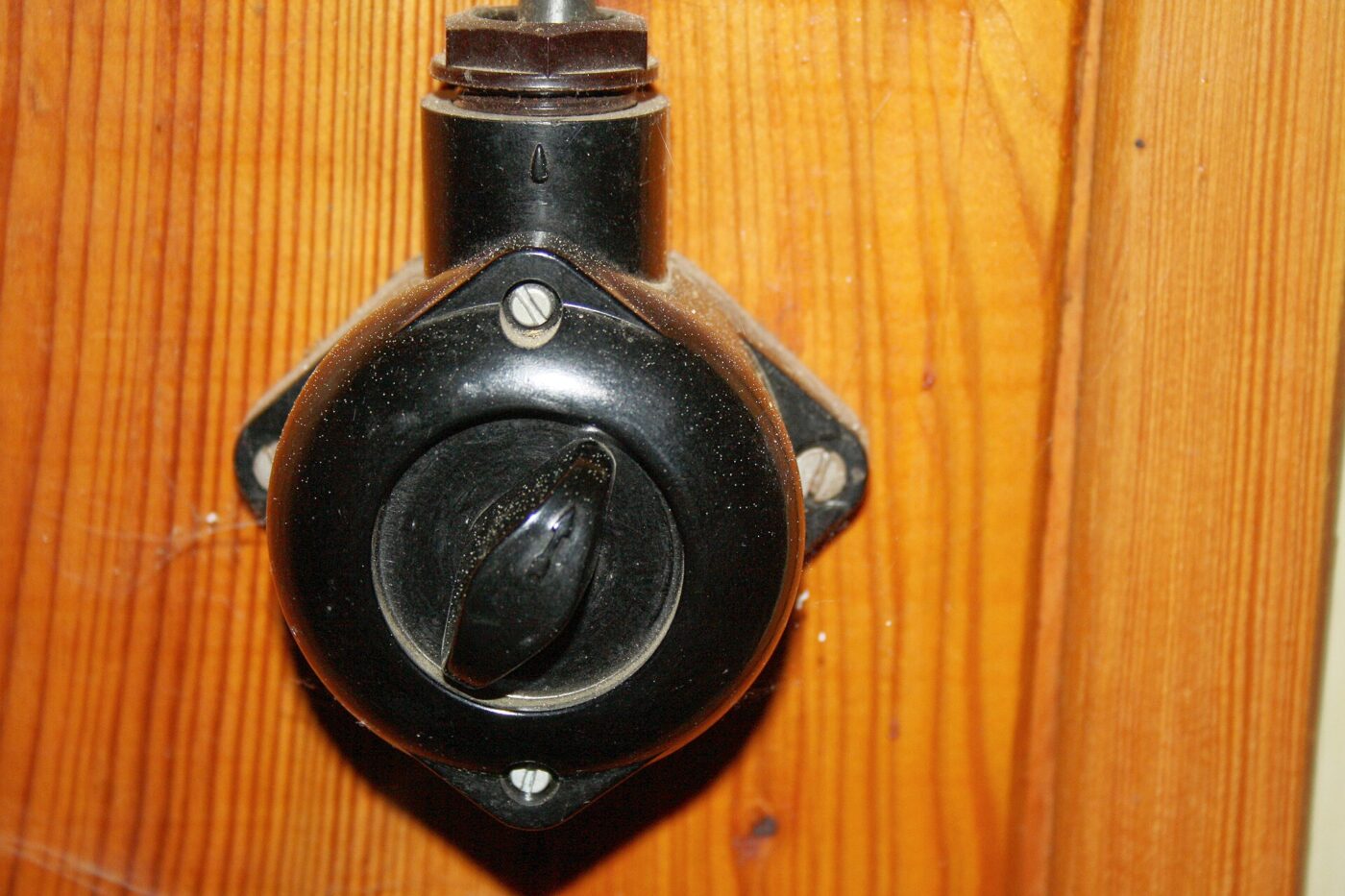 An old black rotary light switch screwed onto a varnished wooden board