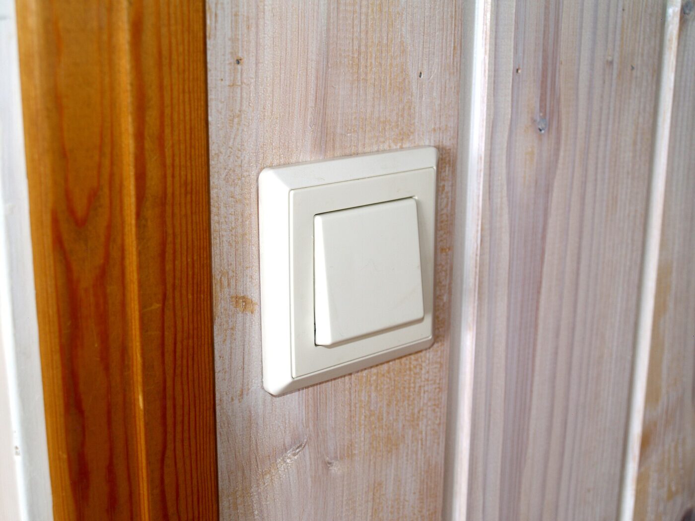 A white rocker light switch on a pale wall beside a wooden door frame