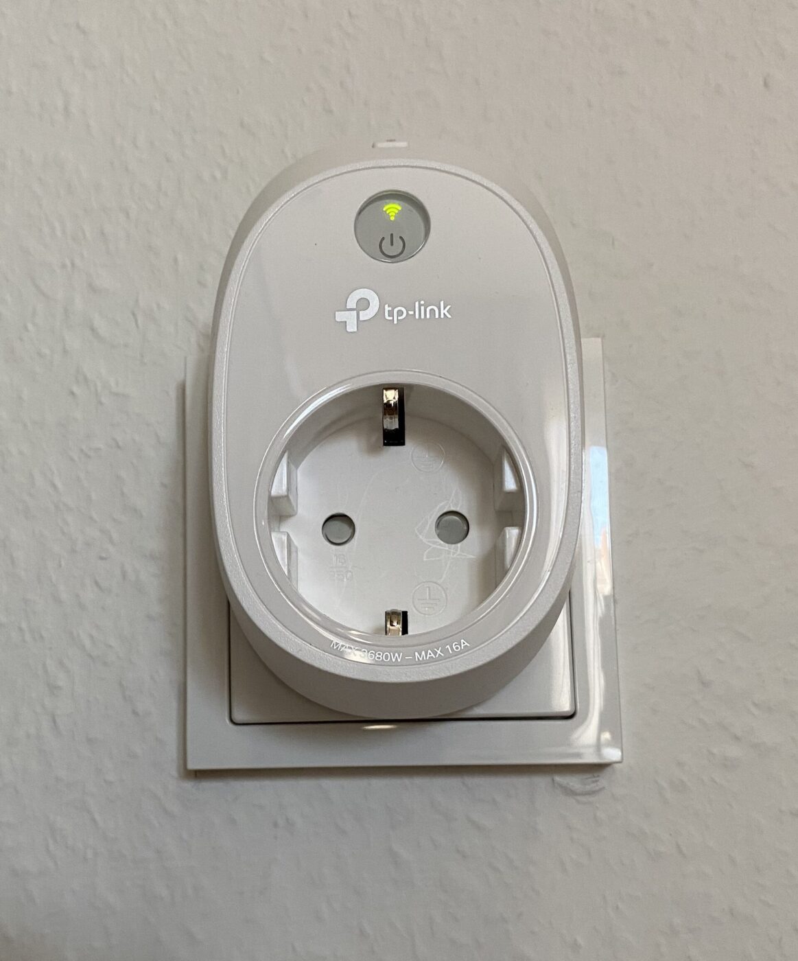 A white smart plug with a power button and status light fitted in a wall outlet.