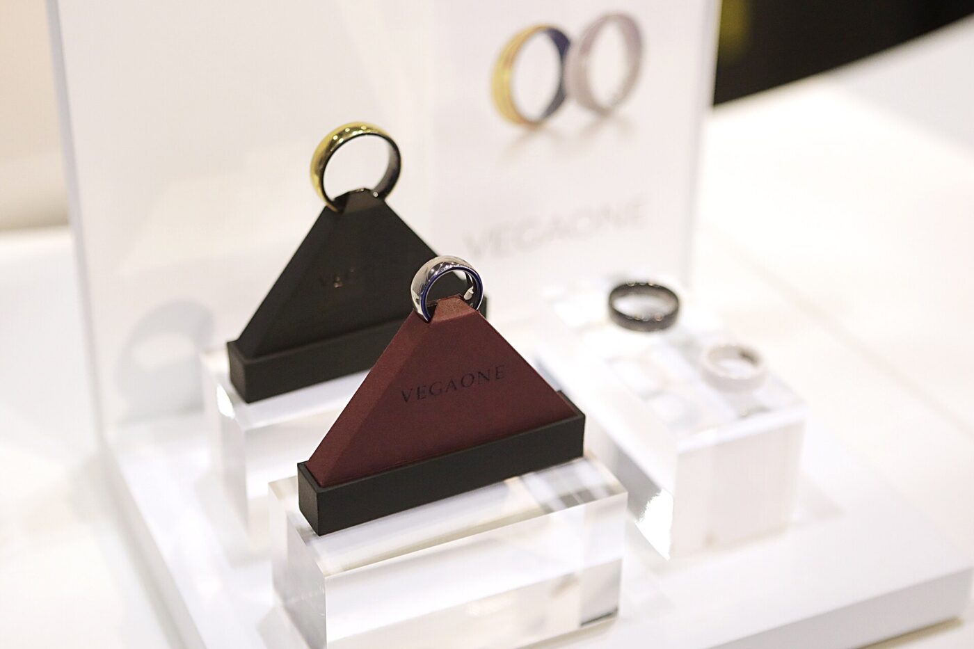 Smart rings in gold, silver and dark finishes on triangular stands at a white product display