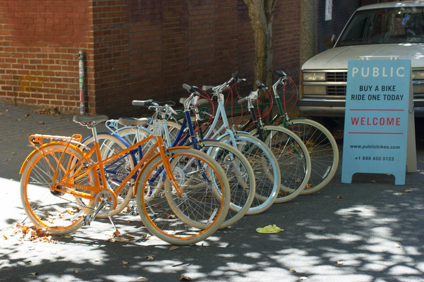 Bicycles lined up for sale outside a shop beside a sidewalk sign that reads Buy a bike, ride one today
